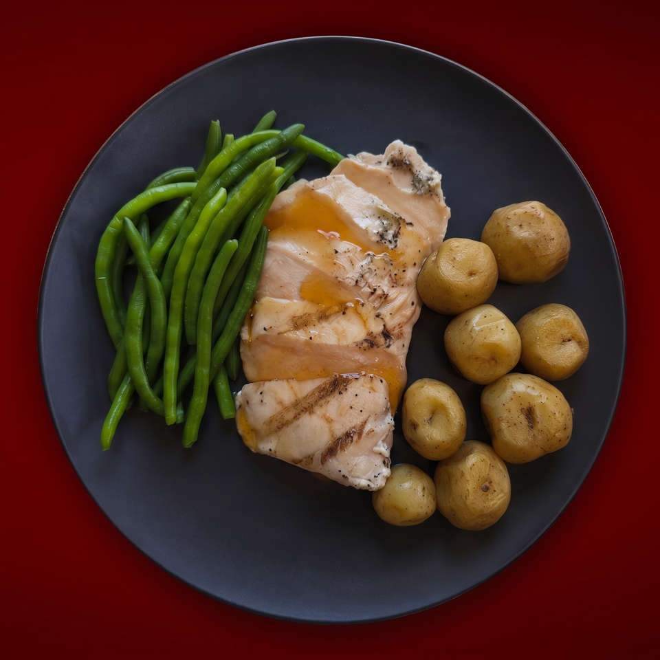 Grilled chicken with green beans and roasted baby potatoes on a dark plate against a deep red background.